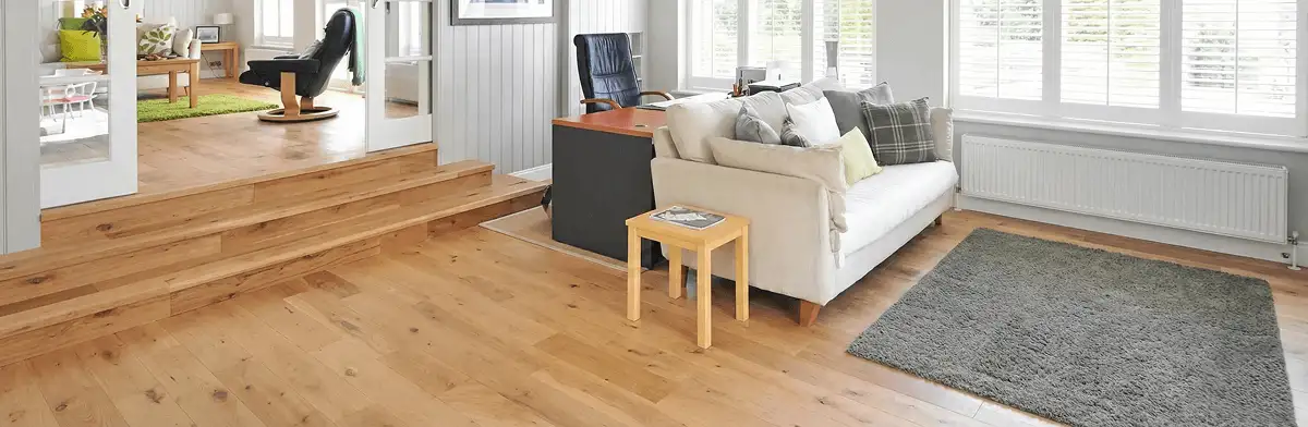 A modern living room with professionally installed laminate flooring, a beige sofa, a small side table, a gray rug, and large windows with white shutters in South Bend, IN